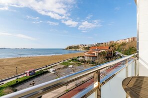 Vista costera desde un balcón con vista a una playa, un estacionamiento y un edificio con techo rojo.