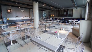 Un restaurante moderno con varias mesas y sillas, una barra con un menú y una escalera que lleva a un nivel superior.