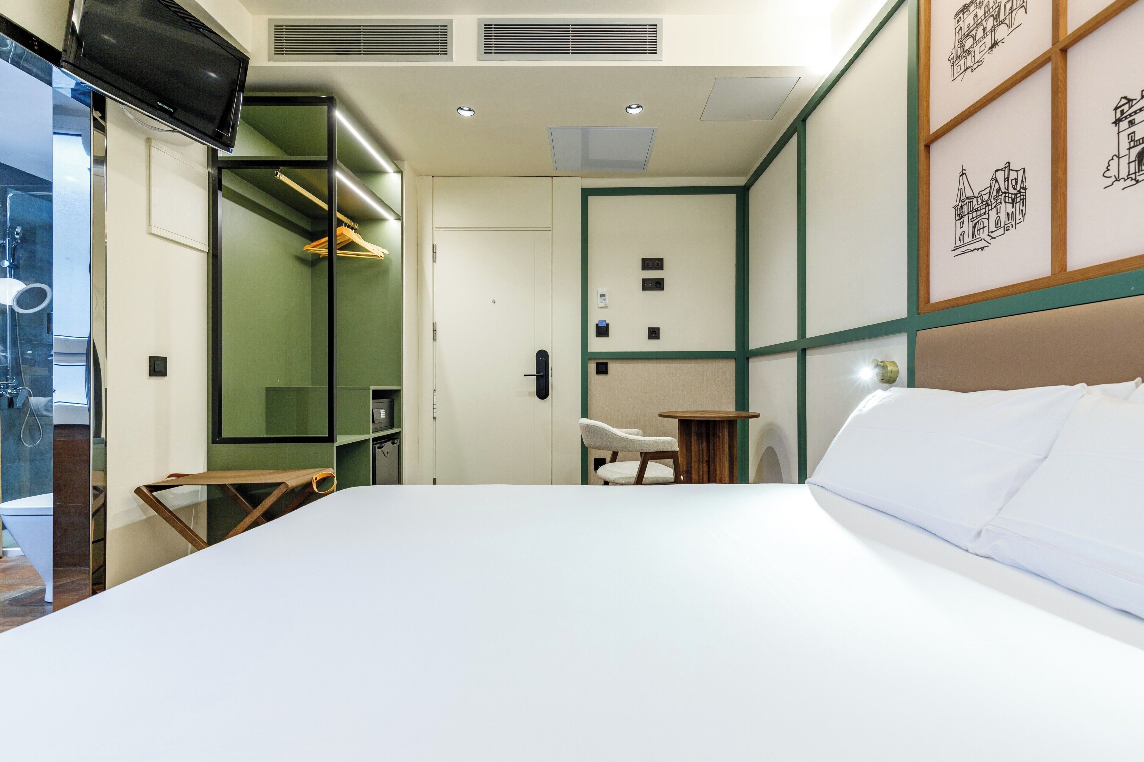 Ein Hotelzimmer mit Bett, Sessel, kleinem Tisch, Fernseher und einer Tür mit Kleiderhaken.