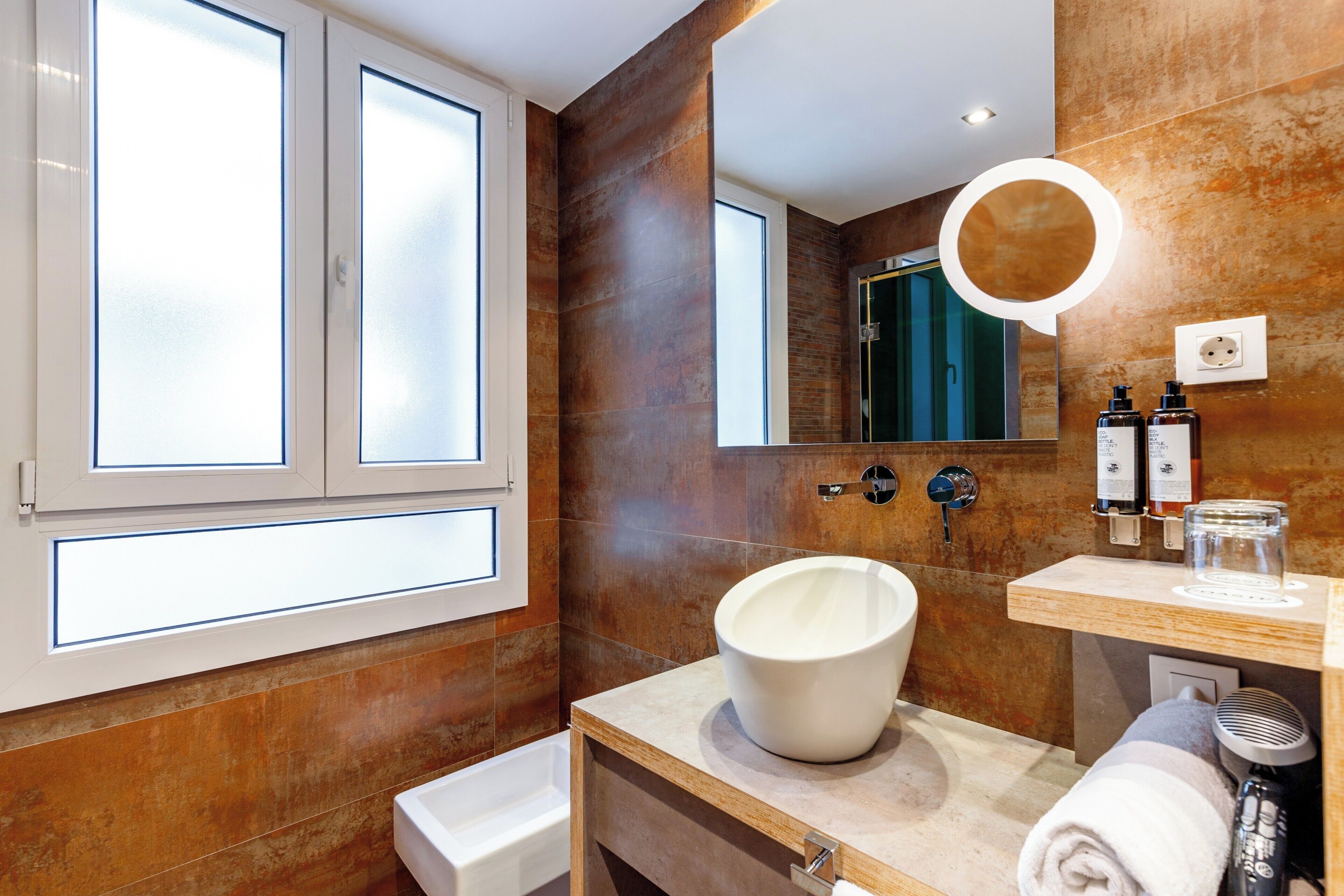 A modern bathroom with a large mirror, a white sink, and a towel on the counter.