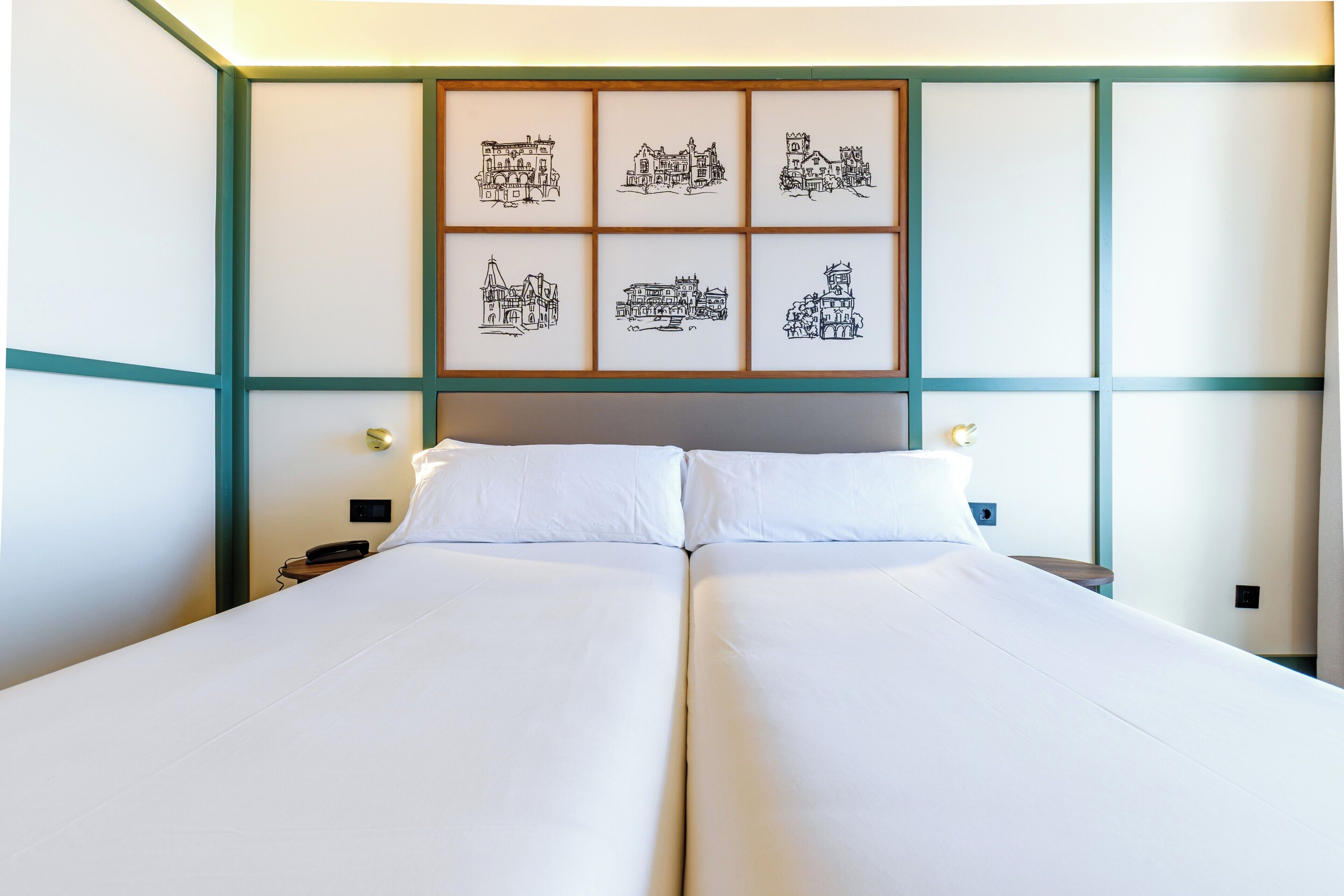 Un lit double avec du linge de lit blanc, une tête de lit ornée d’un tableau encadré, des tables de chevet avec des lampes et un téléphone fixé au mur.