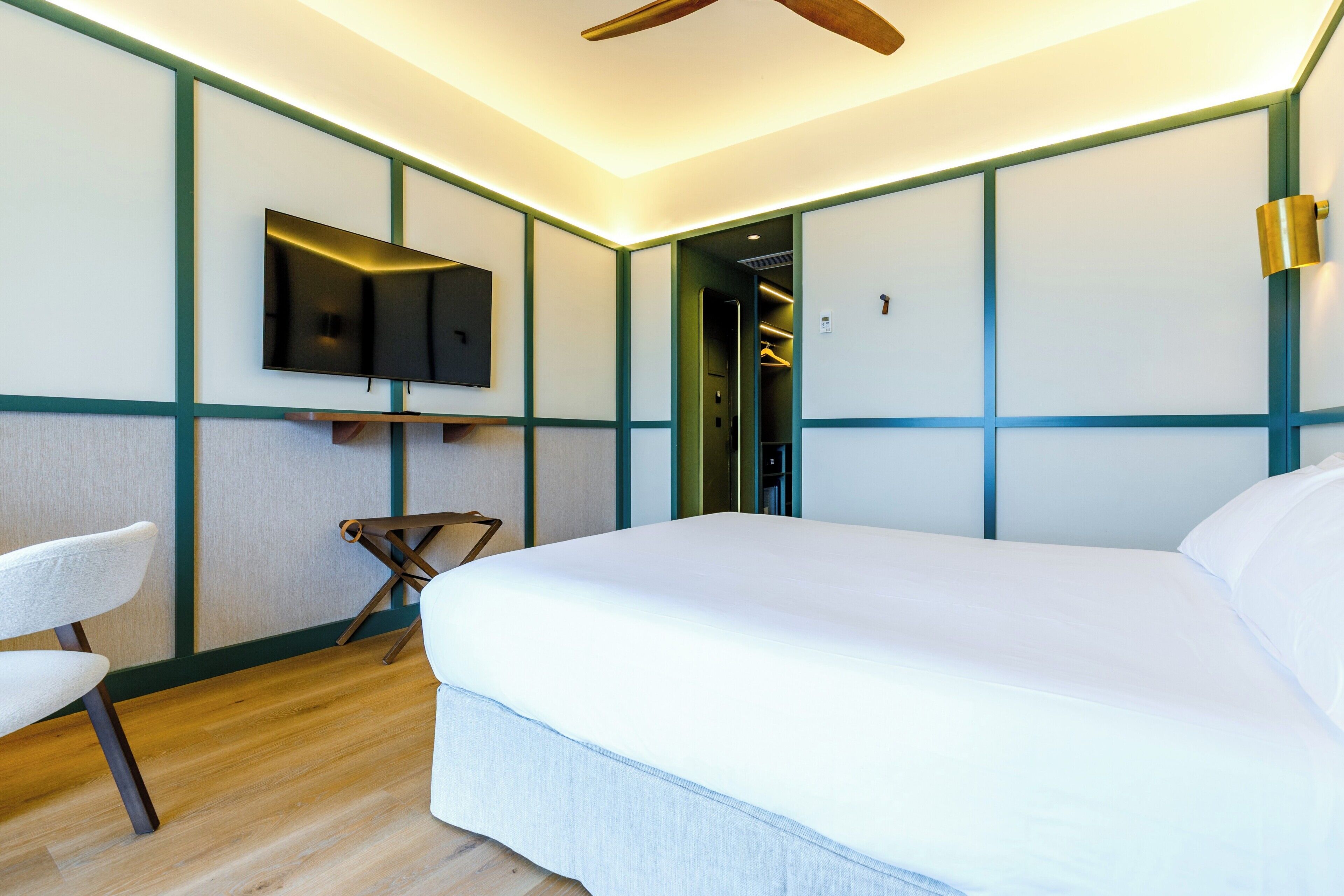Una habitación de hotel moderna con una cama grande, un televisor de pantalla plana en la pared y piso de madera.