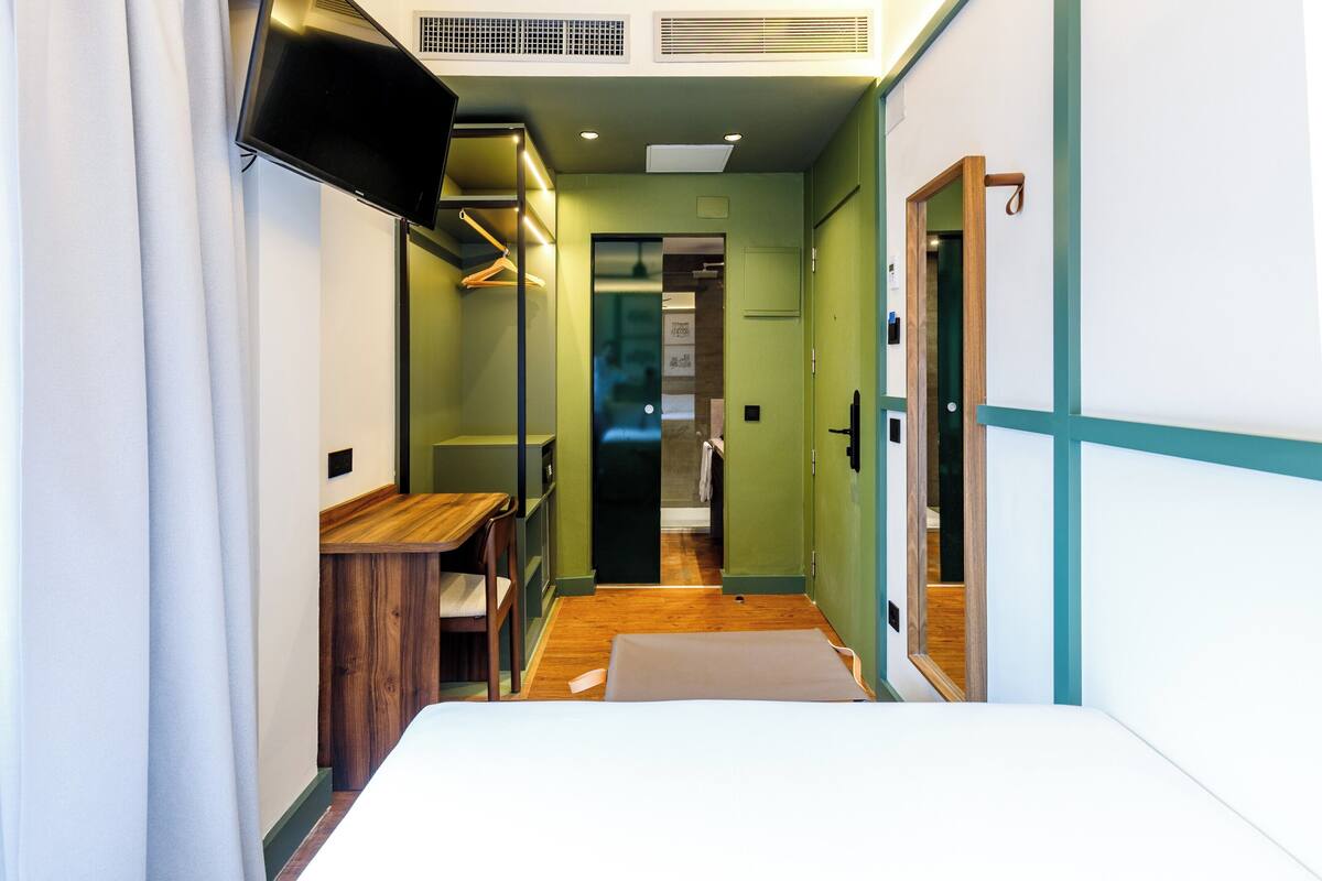 A narrow hallway with a bed, wooden furniture, a TV, and a wardrobe.