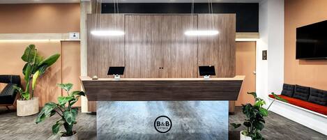 A reception desk with two computer monitors, a logo, and a plant on either side.
