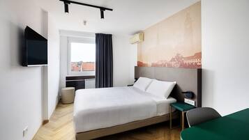Een hotelkamer met een bed, bureau, stoel, televisie en raam met gordijnen.