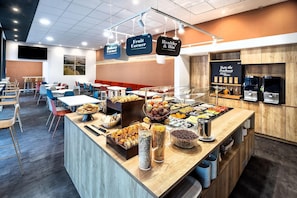 Zona de bufé con diversas opciones de comida, como frutas, pastelería y bebidas.