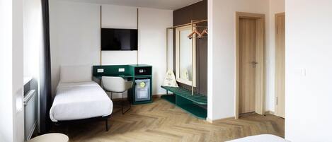 Habitación de hotel con cama, escritorio, silla, armario, espejo y radiador.