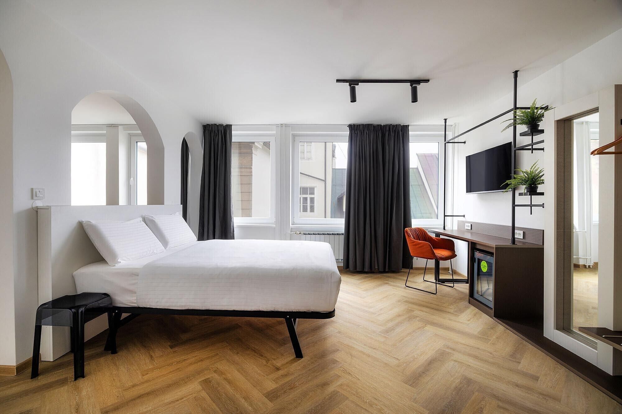 A modern bedroom with a bed, a desk, a chair, a TV, and a window with curtains.