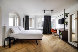 Un dormitorio moderno con cama, escritorio, silla, televisión y ventana con cortinas.