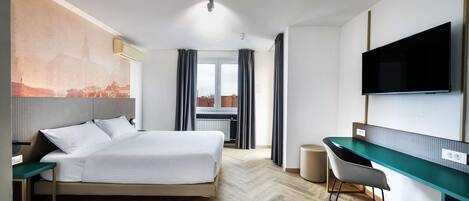 A hotel room with a bed, a desk, a chair, a television, and a view of a cityscape.