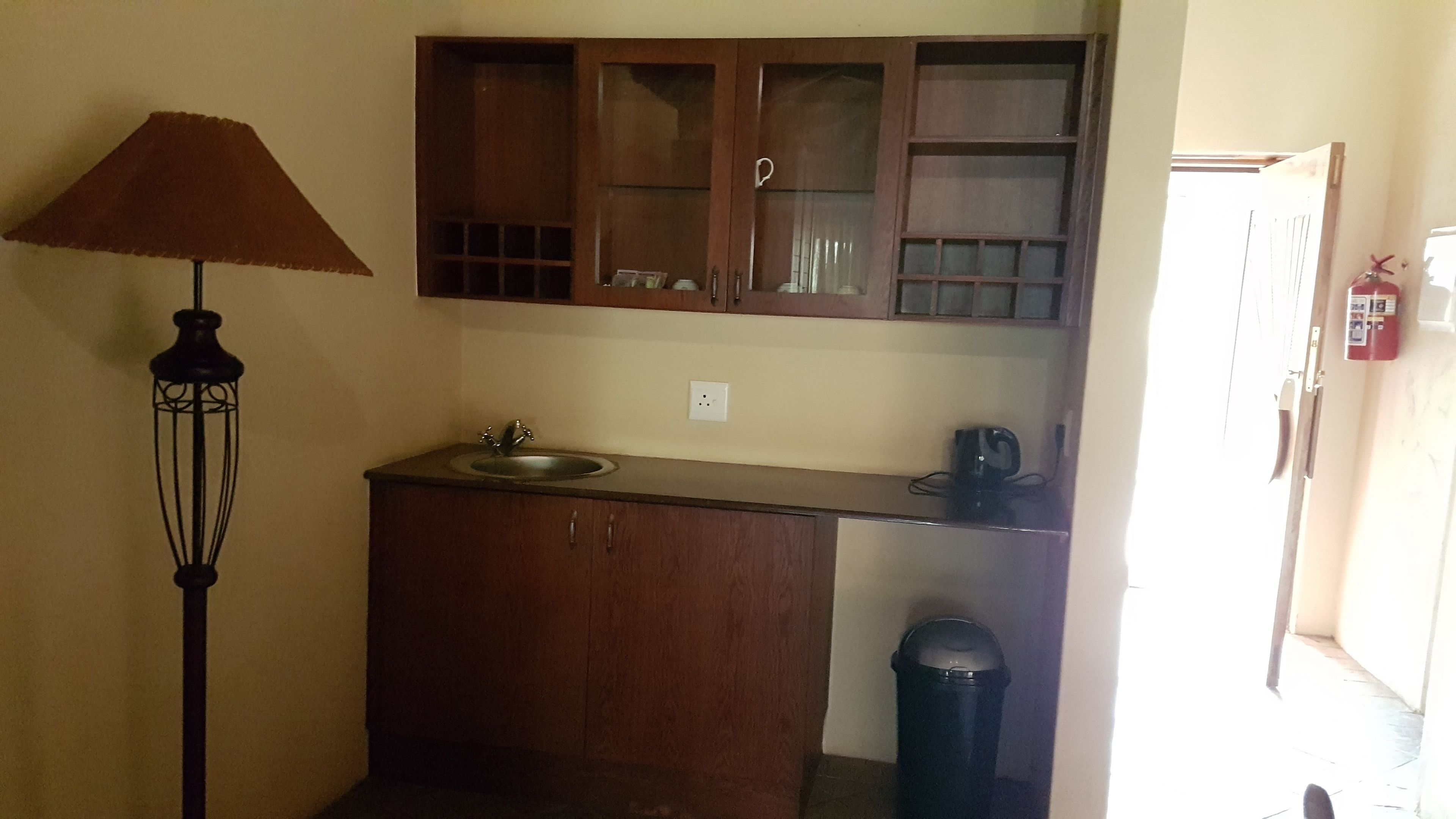 Cocina compacta con un lavamanos, una cafetera, un cubo de basura y un armario sobre la encimera.