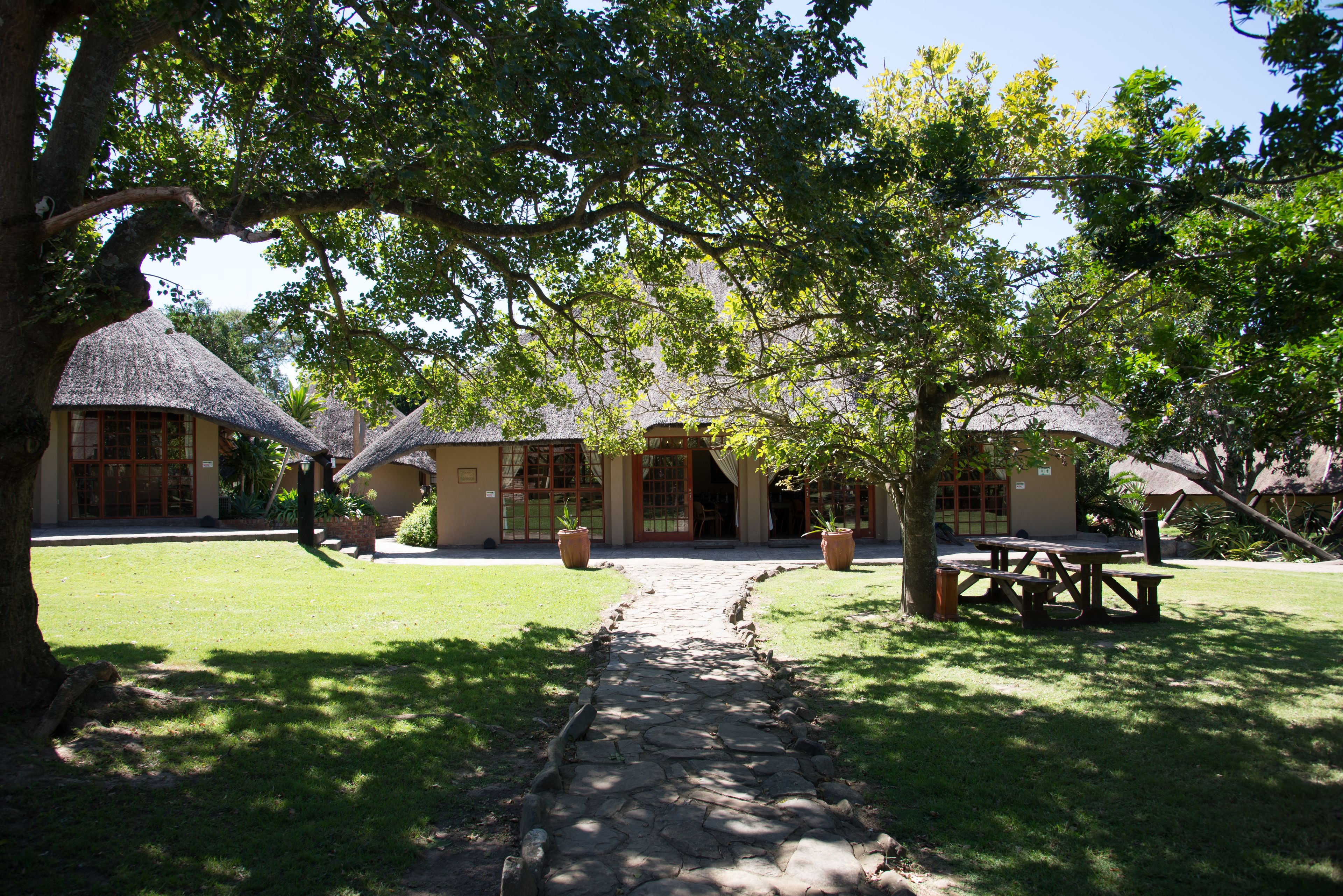 A pathway leading to a building with thatched-roof structures and potted plants.
