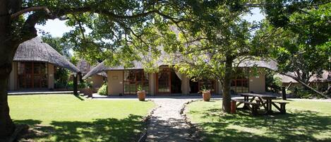 A pathway leading to a building with thatched-roof structures and potted plants.