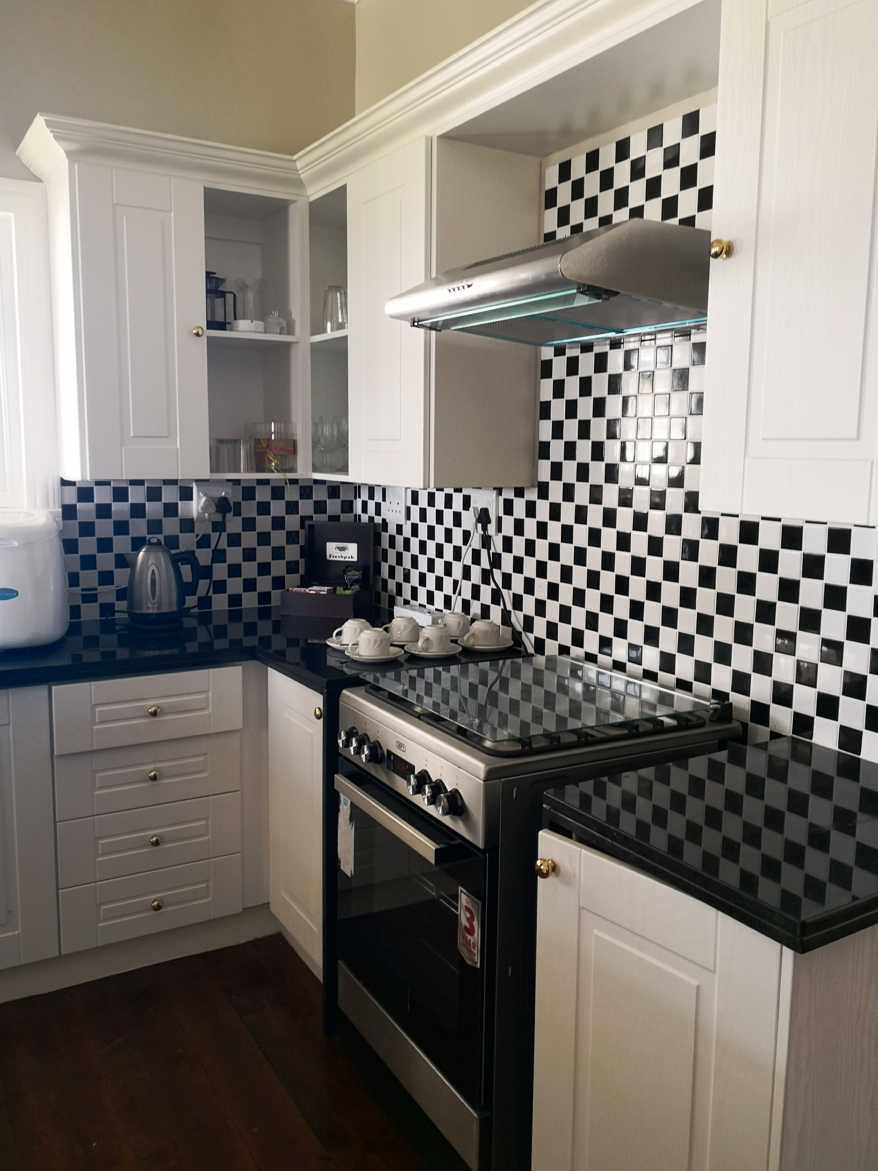 A kitchen with a black and white checkered backsplash, white cabinets, a black stove, and a coffee maker.