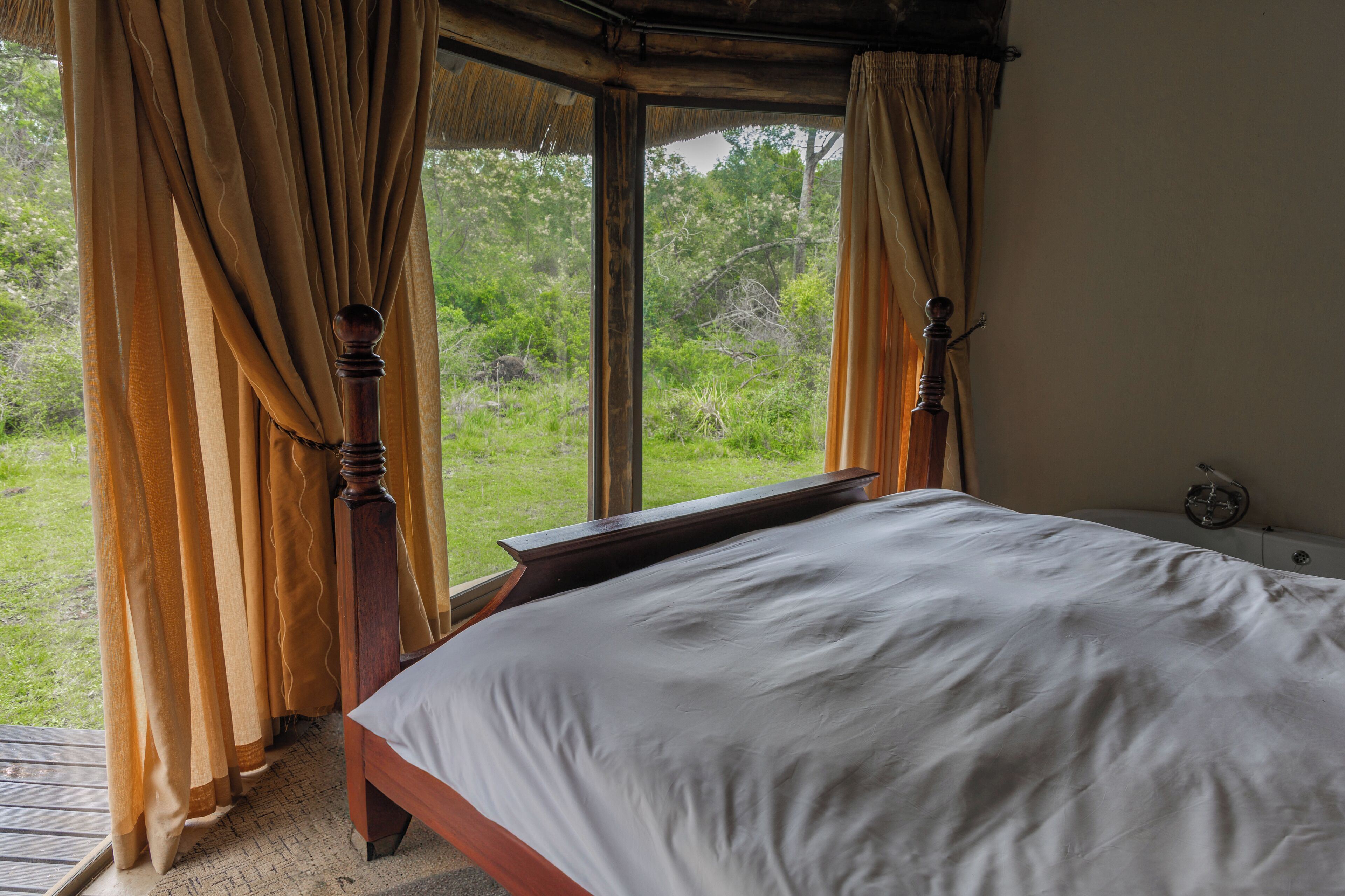 Un dormitorio con cama, cabecero de madera, cortinas y vista a zonas verdes.