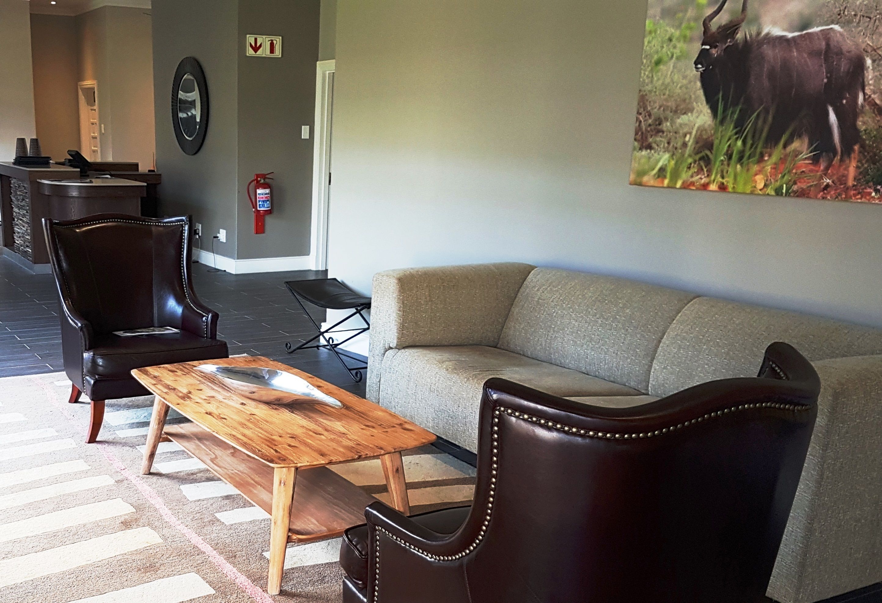 A living room with a sofa, two leather chairs, a wooden coffee table, and a painting of a buffalo on the wall.