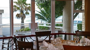 A dining table set for six with chairs, a view of the ocean, and palm trees outside. - Premier Hotel Regent (East London)