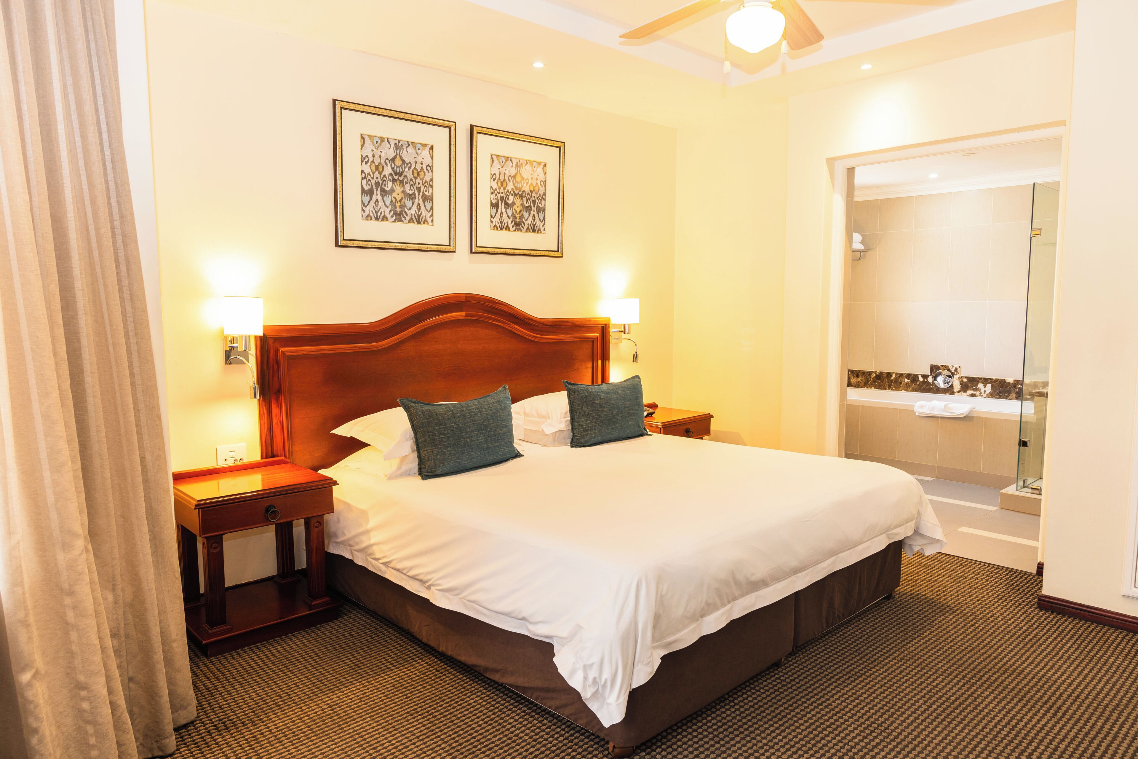 Habitación de hotel con una cama grande, dos mesitas de noche, una lámpara de pared y zona de ducha.