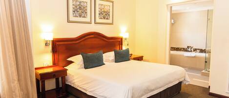 Habitación de hotel con una cama grande, dos mesitas de noche, una lámpara de pared y zona de ducha.