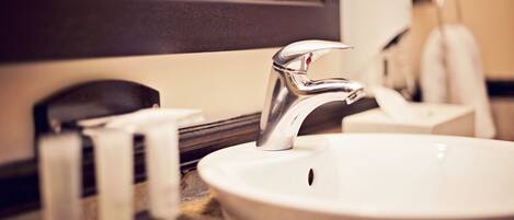 A bathroom sink with a chrome faucet, a mirror above it, and a soap dispenser on the counter.