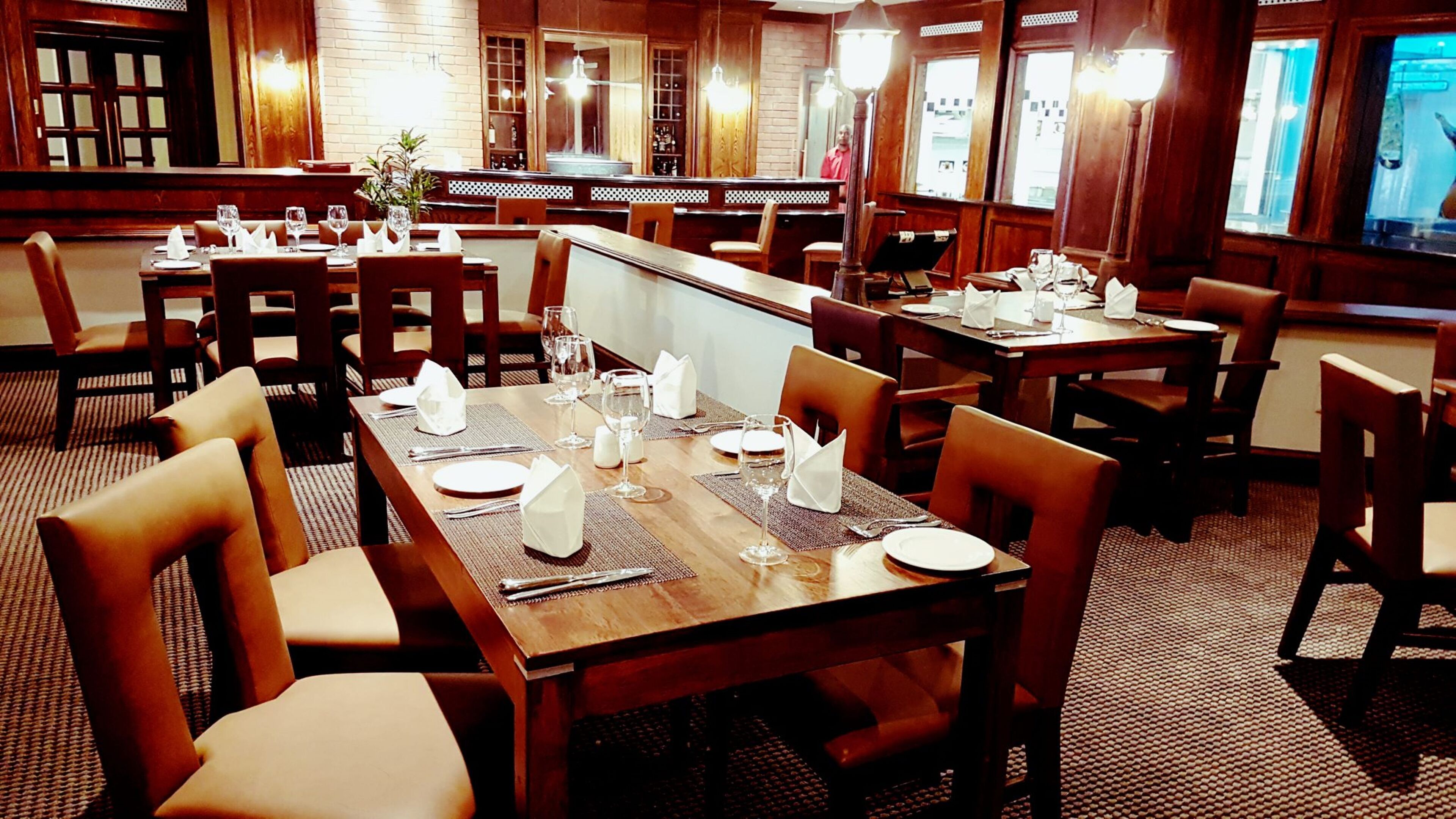 Un restaurante con mesas y sillas de madera, dispuesto con servilletas blancas y cristalería.