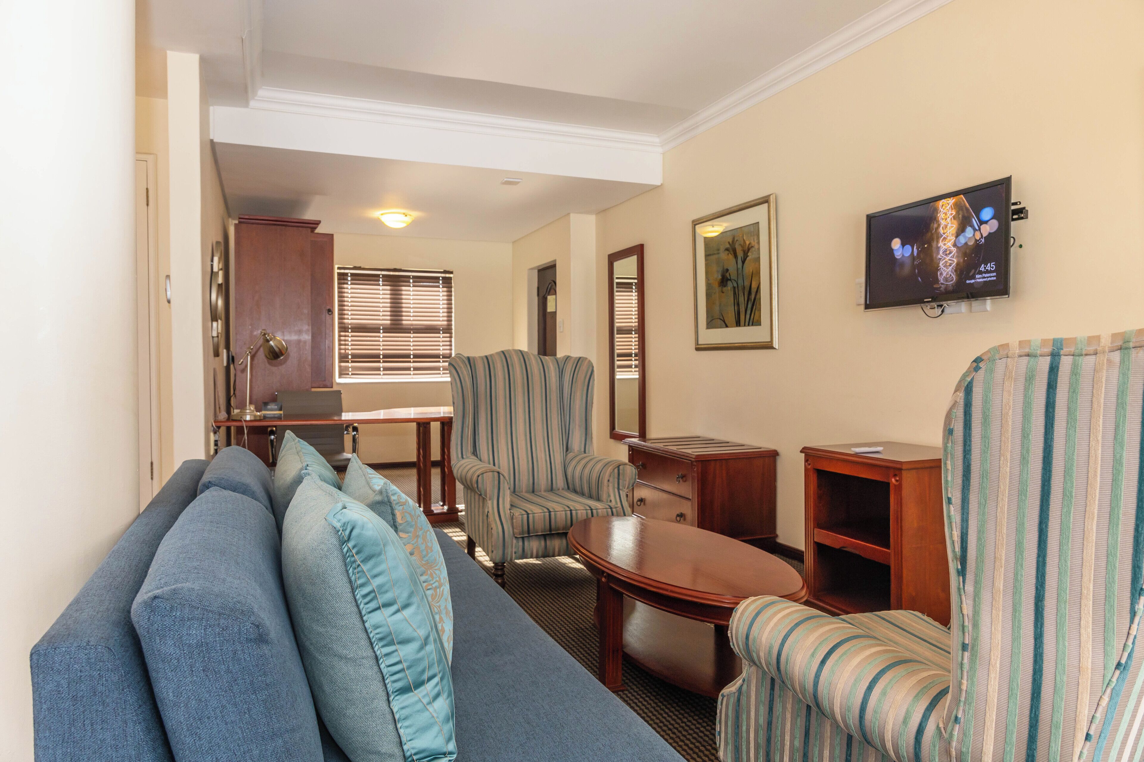 Una sala de estar con un sofá, sillones, una mesa de centro y un televisor montado en la pared.