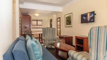 Una sala de estar con un sofá, sillones, una mesa de centro y un televisor montado en la pared.