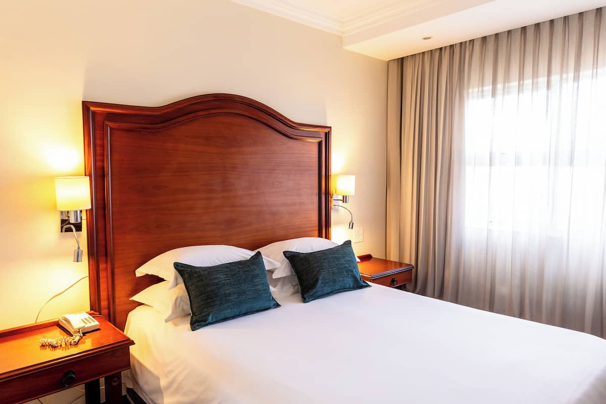 A hotel room with a large bed, two bedside lamps, a nightstand with a phone, and a window with curtains.