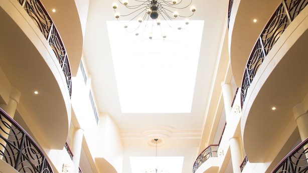 A multi-level atrium with a central staircase, ornate railings, and a chandelier. - Premier Hotel Regent (East London)