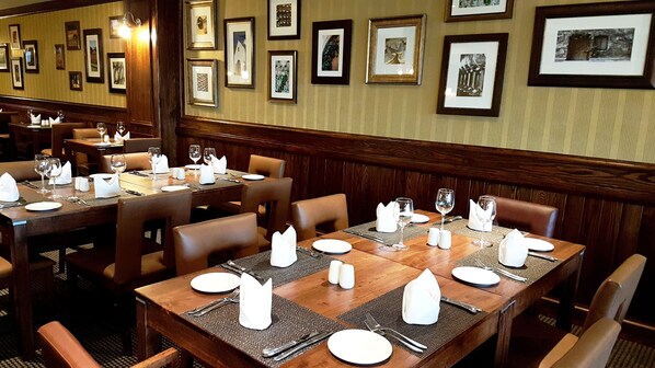 A restaurant with wooden tables and chairs, neatly set with white napkins, plates, and cutlery.