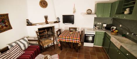 A cozy living room with a sofa, a dining table, and a fireplace. There is a kitchen area with green cabinets and a tiled floor.