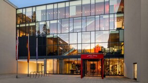 Un bâtiment moderne doté de grandes fenêtres en verre, d’une entrée bien visible et d’une enseigne indiquant « VIENNA HOUSE ».