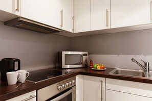 A modern kitchen with white cabinets, a stainless steel microwave, an electric stove, and a sink. - Vienna House Easy by Wyndham Stuttgart (Stuttgart)