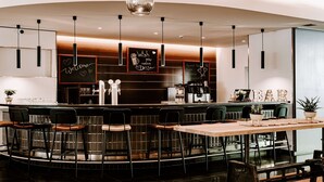 Un espace bar moderne doté d’un comptoir incurvé, de plusieurs tabourets et de luminaires suspendus.