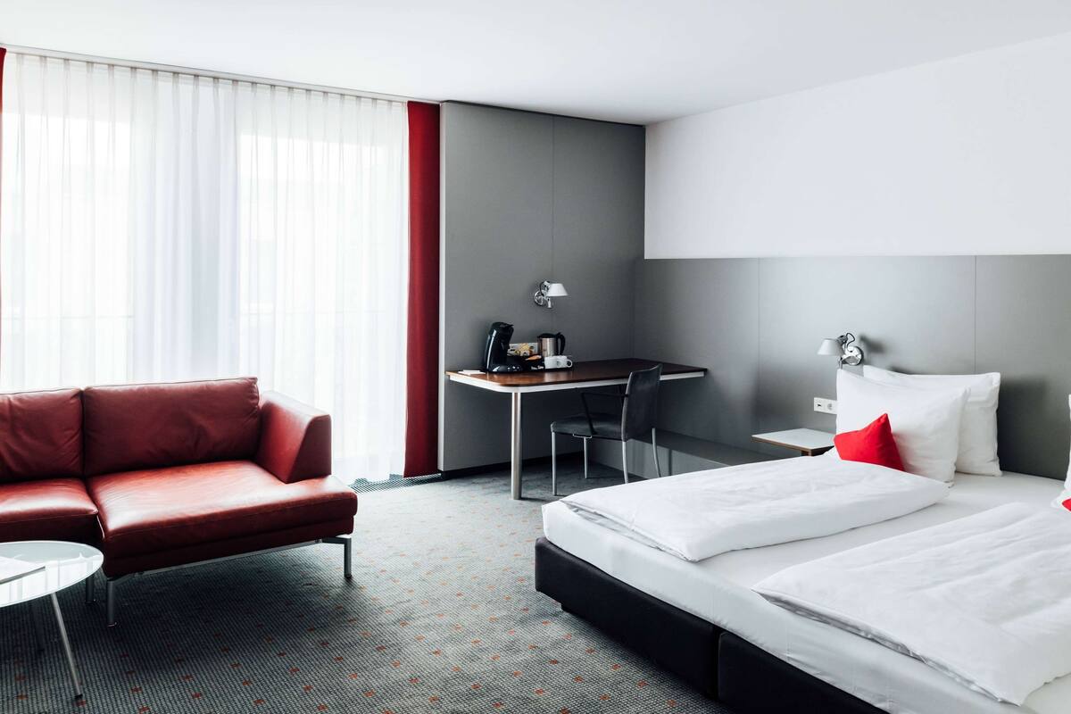 A hotel room with a bed, a desk, a chair, and a sofa.