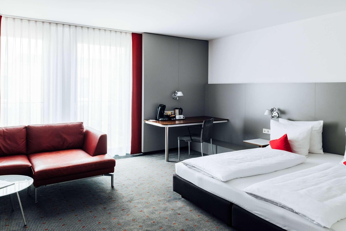 A hotel room with a bed, a desk, a chair, and a sofa.