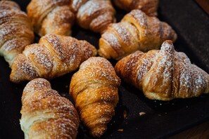 A collection of golden-brown croissants dusted with powdered sugar, arranged on a dark surface. - Vienna House Easy by Wyndham Stuttgart (Stuttgart)