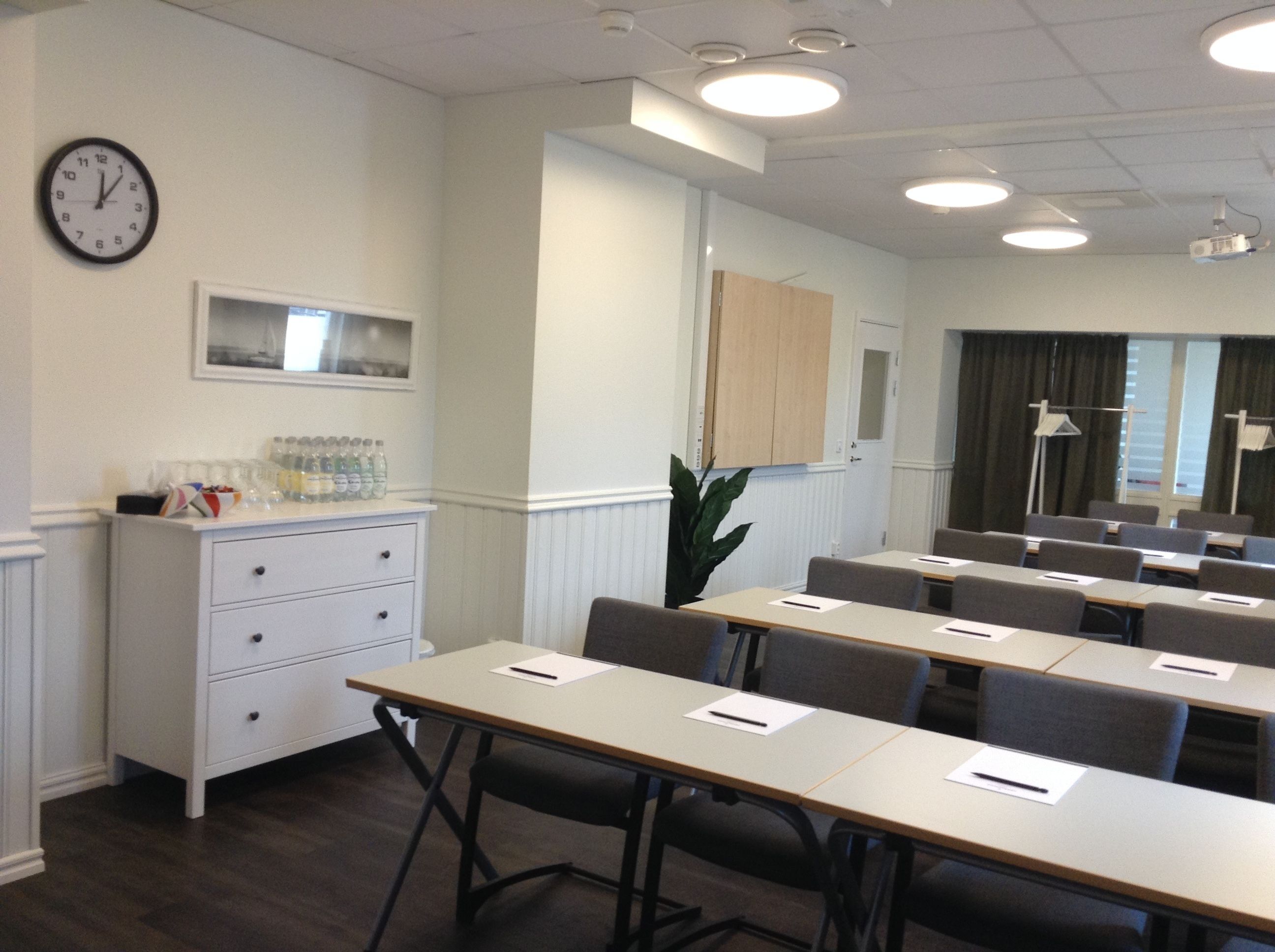 A conference room with tables, chairs, a clock, a water dispenser, and a plant.