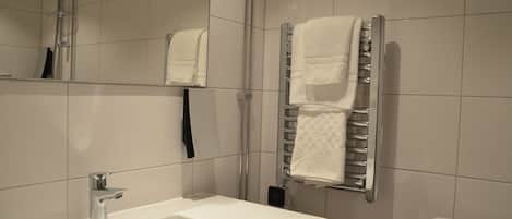 Un bagno moderno con un lavandino bianco, box doccia in vetro e porta asciugamani con asciugni piegati.