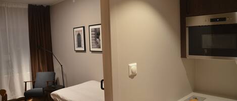 Habitación de hotel con cama, escritorio, silla, lámpara, ventana con cortinas y microondas.
