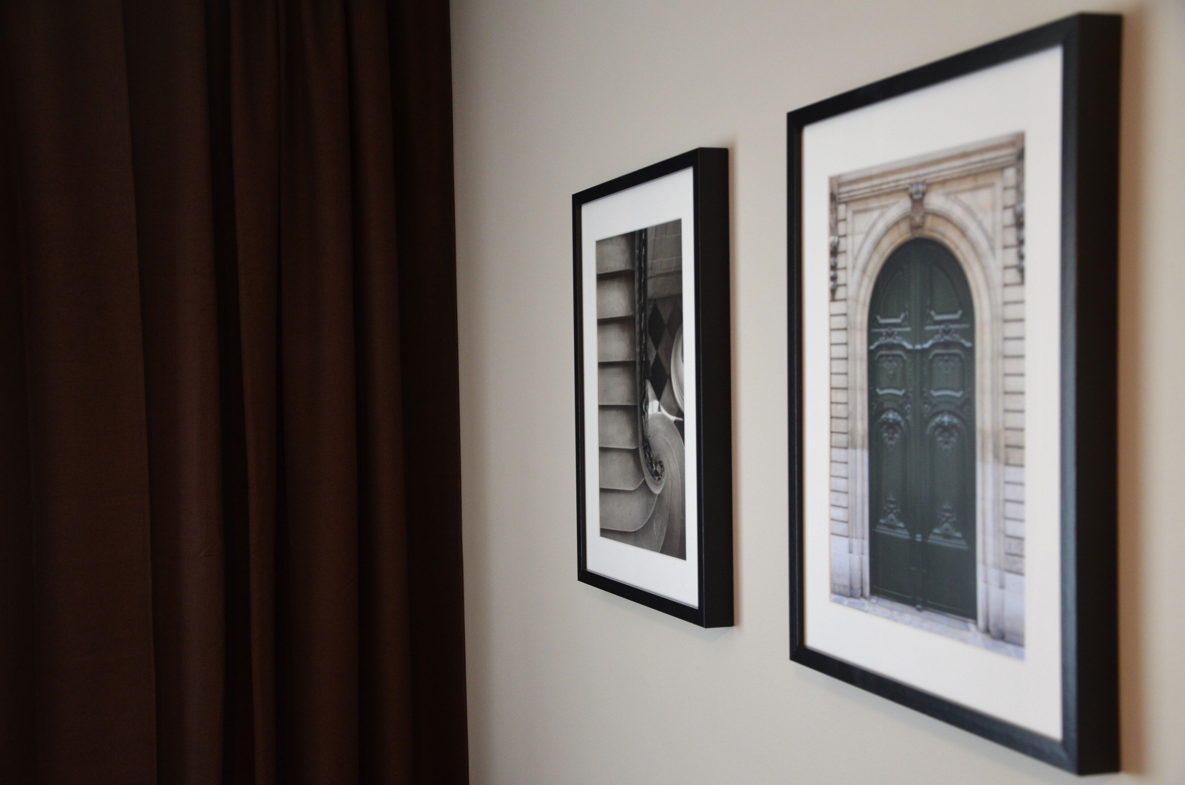 Two framed pictures on a wall, one depicting a building facade and the other a close-up of a door.