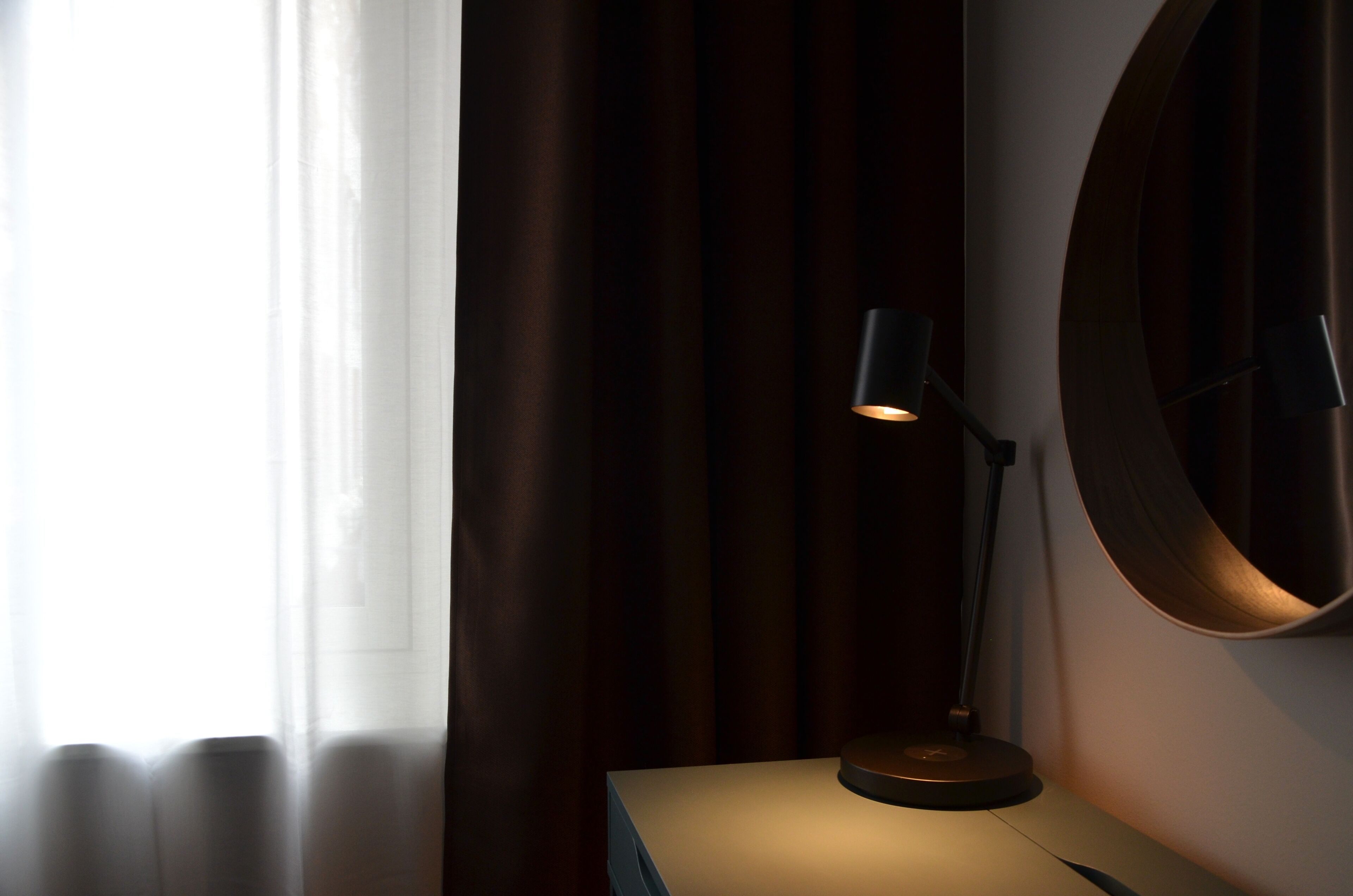 A room with a desk, a lamp, and a large mirror on the wall.