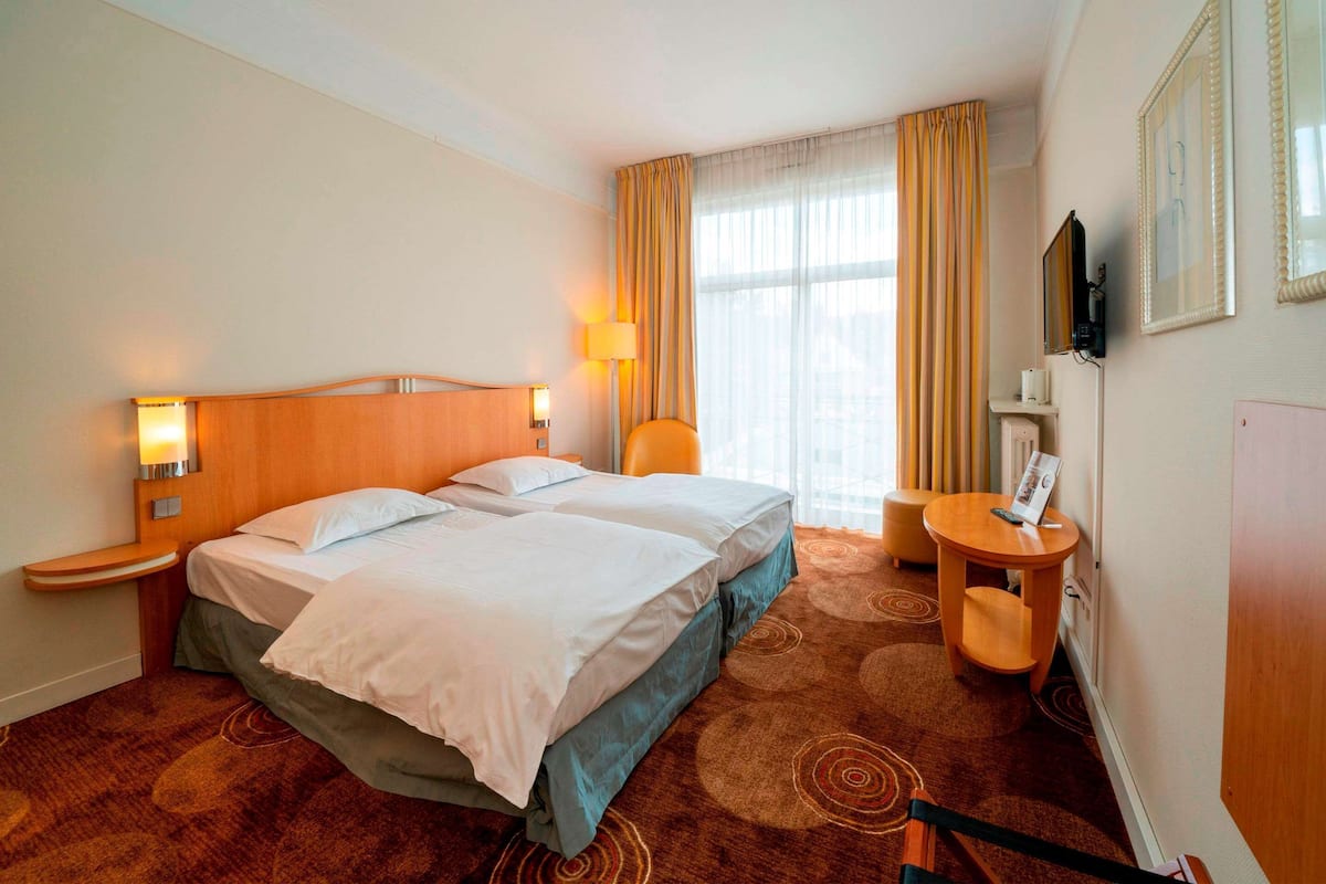 Ein Hotelzimmer mit zwei Betten, einem Schreibtisch, einem Stuhl, einem Fernseher und einem Fenster mit Vorhängen.