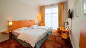 A hotel room with two beds, a desk, a chair, a TV, and a window with curtains.