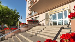 A grand hotel entrance with a staircase leading to the entrance, surrounded by red flowers.