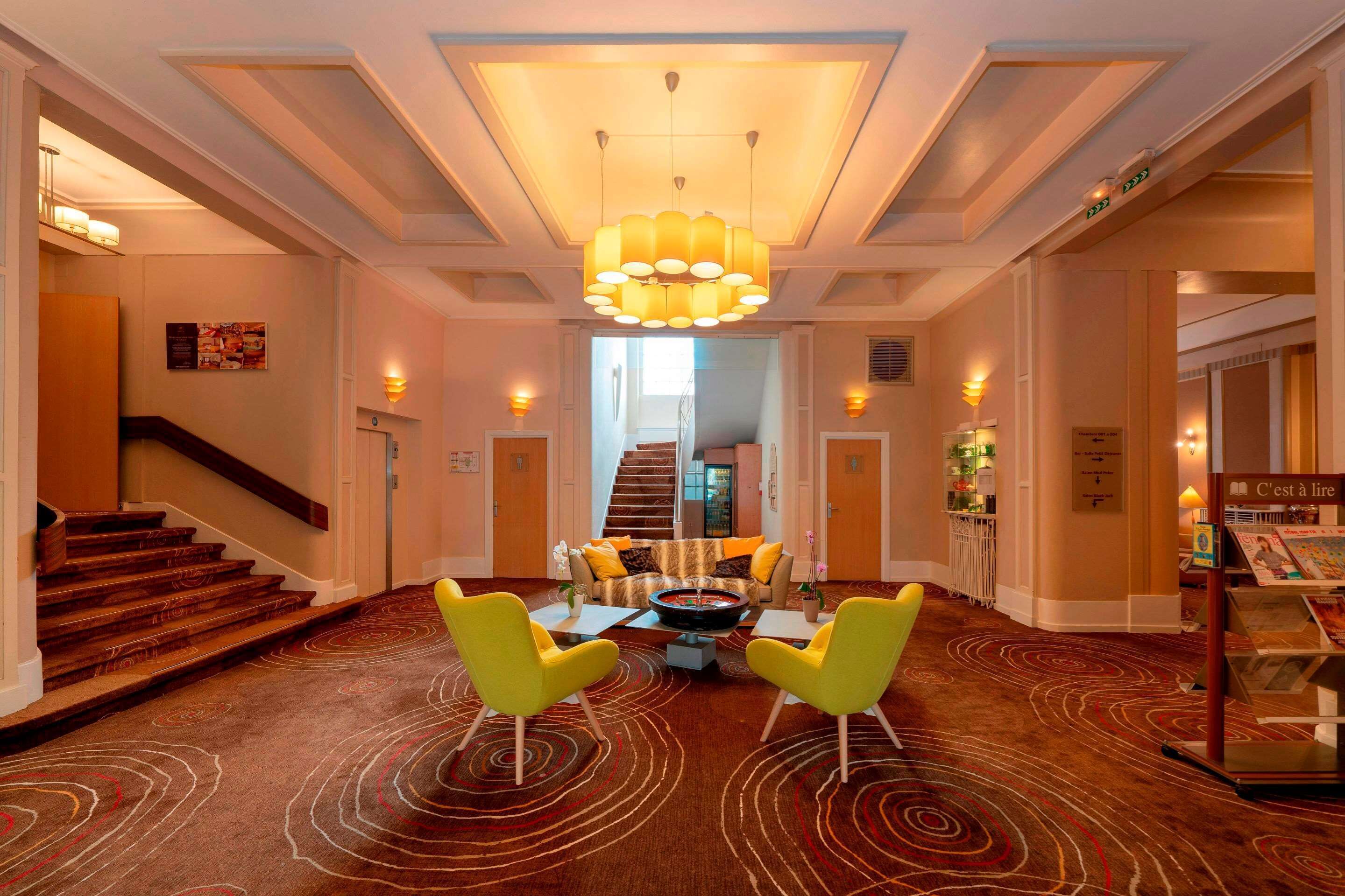 A hotel lobby with a central seating area, a staircase, and a reception desk.