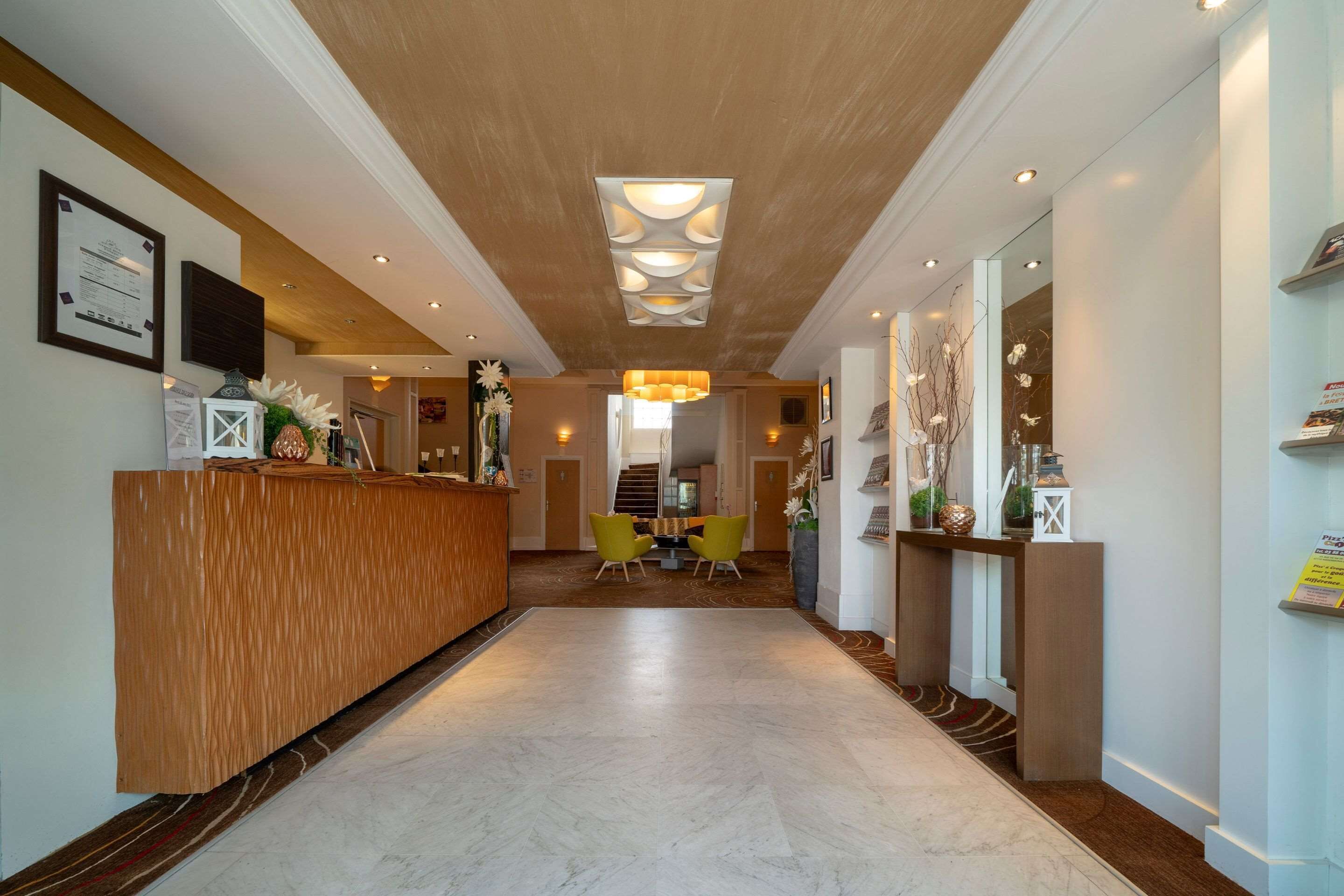 Zona de recepción de un hotel con un mostrador de madera, suelo de mármol y una escalera al fondo.