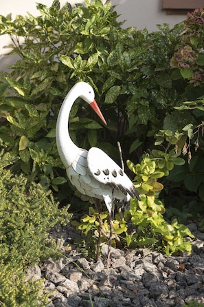 Una estatua de pájaro en un jardín con follaje verde y rocas.