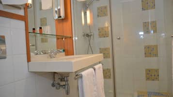 A bathroom with a glass shower enclosure, a white sink with a mirror, and a tiled floor.