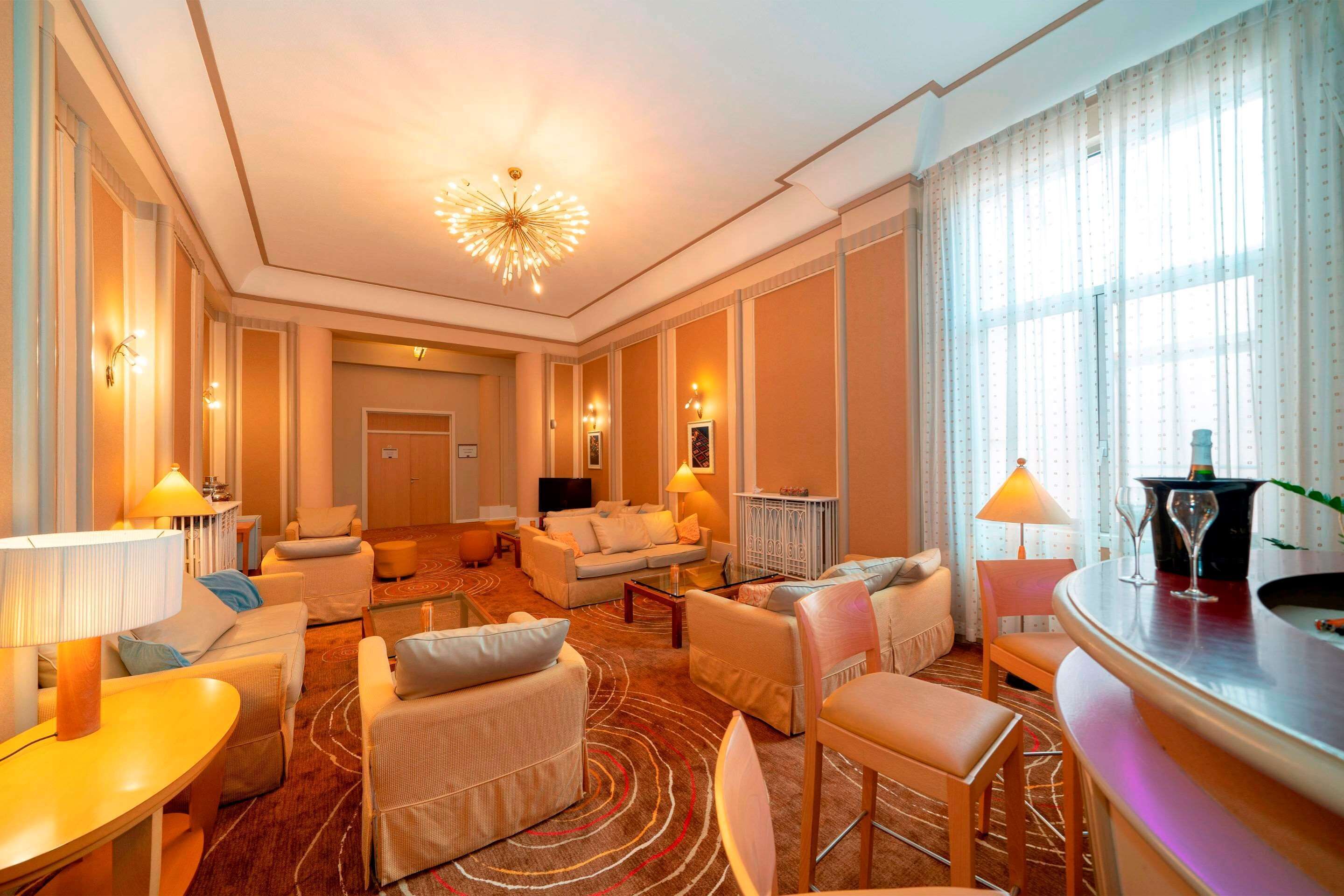 A spacious hotel lobby with a modern chandelier, comfortable seating areas, and a bar.